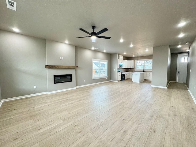 6003 SW Desert Ave, Bentonville, AR 72713 - unfurnished living room featuring a ceiling fan, light wood finished floors, a glass covered fireplace, recessed lighting, and a textured ceiling