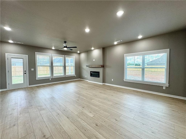 6003 SW Desert Ave, Bentonville, AR 72713 - unfurnished living room featuring a ceiling fan, a glass covered fireplace, wood finished floors, plenty of natural light, and recessed lighting