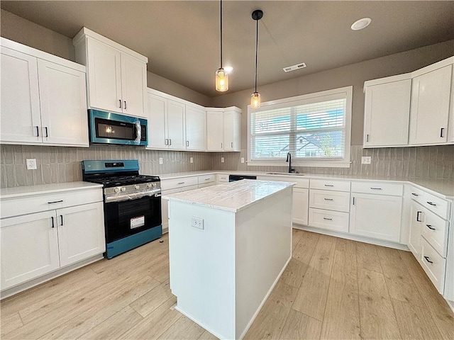 6003 SW Desert Ave, Bentonville, AR 72713 - kitchen with stainless steel appliances, light wood-style floors, a center island, hanging light fixtures, and white cabinetry