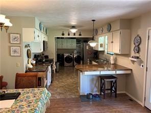411 Natchez Trace St, Harrison, AR 72601 - kitchen featuring washing machine and clothes dryer, a peninsula, a kitchen bar, white cabinets, and decorative light fixtures