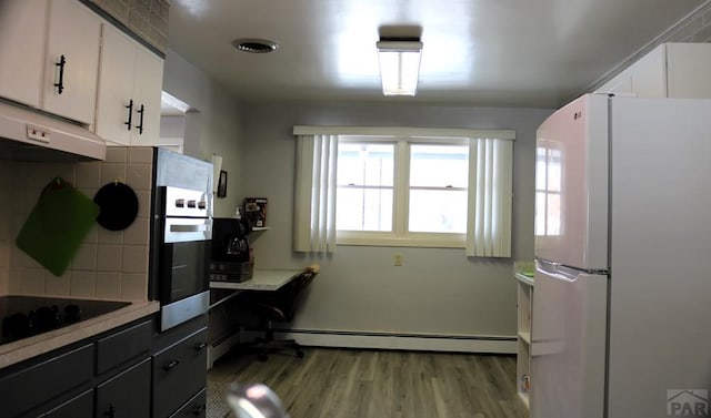 kitchen featuring backsplash, a baseboard heating unit, freestanding refrigerator, white cabinets, and black electric cooktop