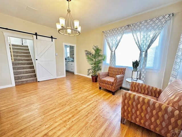 sitting room featuring a chandelier, a barn door, light wood-style flooring, baseboards, and stairs