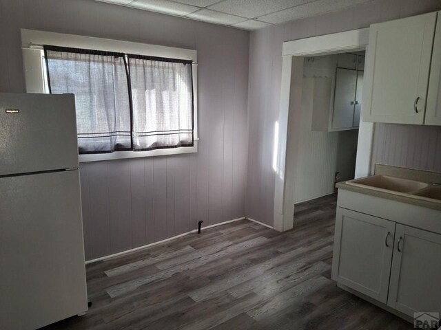 unfurnished dining area with dark wood-style floors, a drop ceiling, and a sink