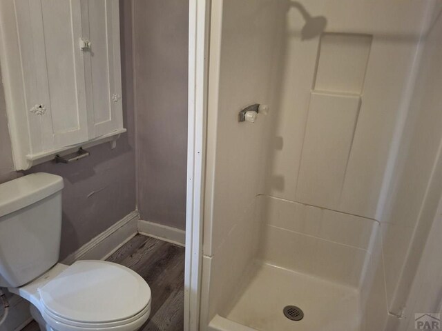 bathroom featuring toilet, a shower stall, baseboards, and wood finished floors