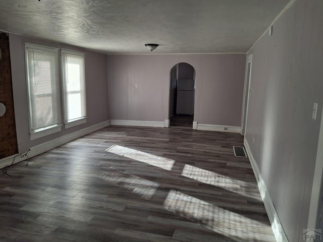 unfurnished room featuring dark wood-type flooring, arched walkways, visible vents, and baseboards