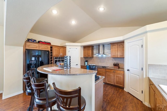 1037 W Desert Sage Dr, Pueblo West, CO 81007 - kitchen with wall chimney exhaust hood, a breakfast bar area, dark wood-style floors, vaulted ceiling, and a kitchen island with sink