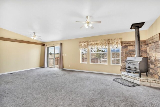 unfurnished living room featuring carpet floors, a wood stove, baseboards, and a ceiling fan