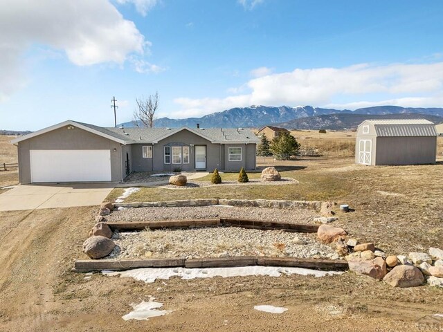 ranch-style house with an outbuilding, an attached garage, a mountain view, driveway, and a shed