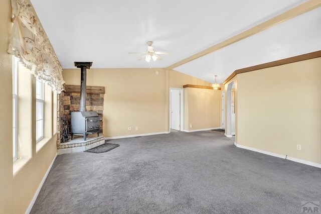 unfurnished living room with lofted ceiling with beams, a wood stove, baseboards, and dark carpet