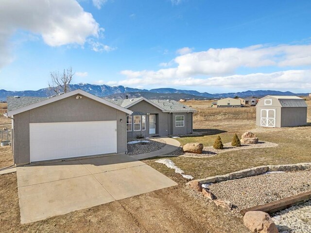 single story home with concrete driveway, a mountain view, a shed, and stucco siding