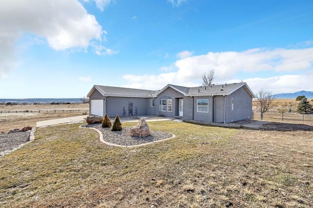 view of front of property with an attached garage, a rural view, fence, and stucco siding