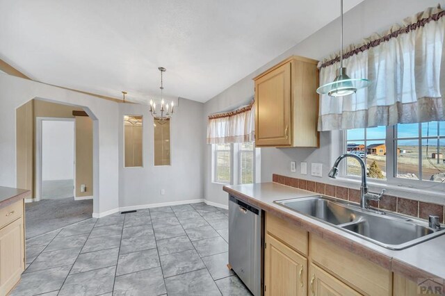 kitchen with arched walkways, pendant lighting, stainless steel dishwasher, light brown cabinetry, and a sink