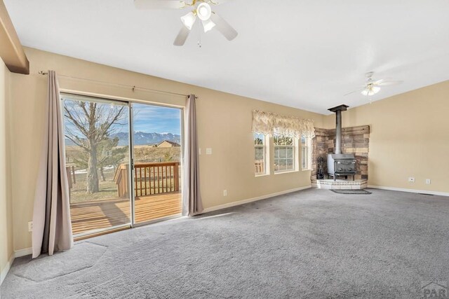 unfurnished living room with a wood stove, ceiling fan, and carpet flooring