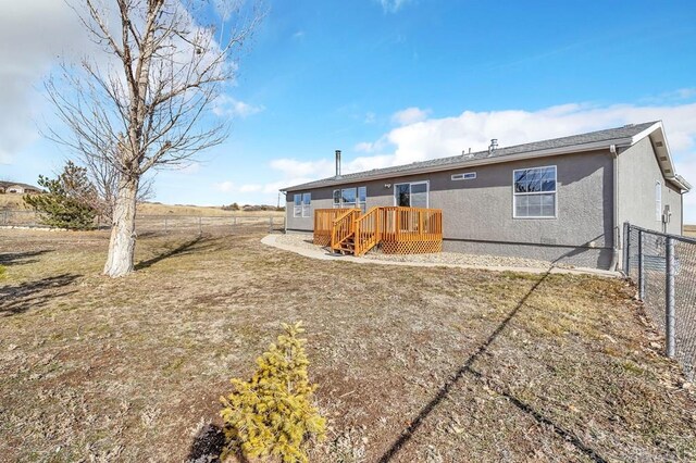 rear view of house with a yard, fence, a wooden deck, and stucco siding