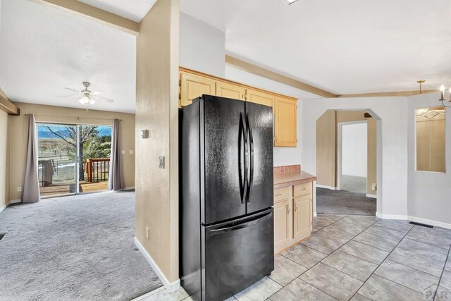 kitchen featuring arched walkways, light colored carpet, light countertops, freestanding refrigerator, and light brown cabinetry