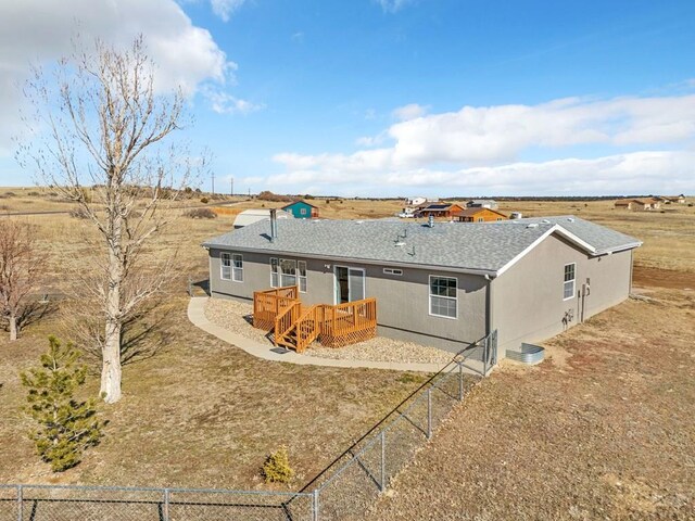 rear view of house with roof with shingles, fence, a deck, and a rural view