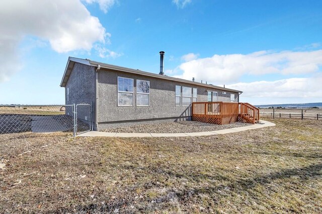 rear view of property with a lawn, fence, a deck, and stucco siding