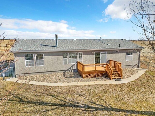 rear view of house featuring fence, roof with shingles, a lawn, a wooden deck, and stucco siding