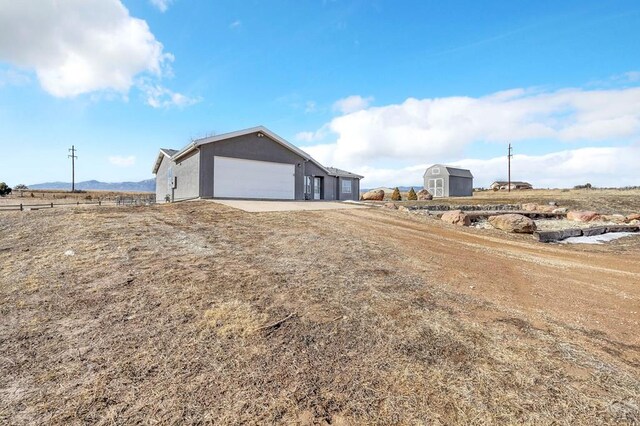 exterior space featuring dirt driveway, a storage unit, fence, a garage, and a rural view