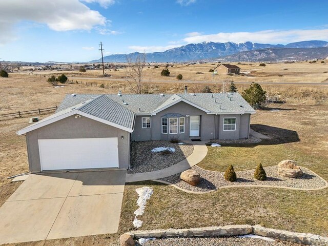 single story home featuring stucco siding, a front yard, a mountain view, a garage, and driveway