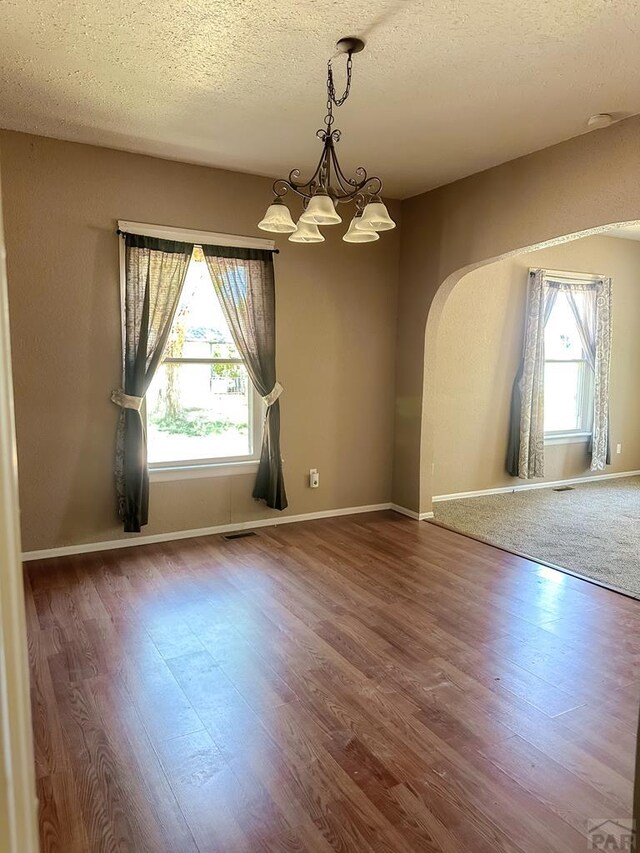 1202 Belleview Ave, La Junta, CO 81050 - spare room featuring a chandelier, a textured ceiling, wood finished floors, and arched walkways