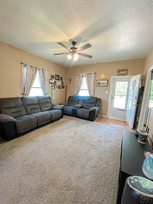 living area featuring light colored carpet, a healthy amount of sunlight, ceiling fan, and a textured ceiling