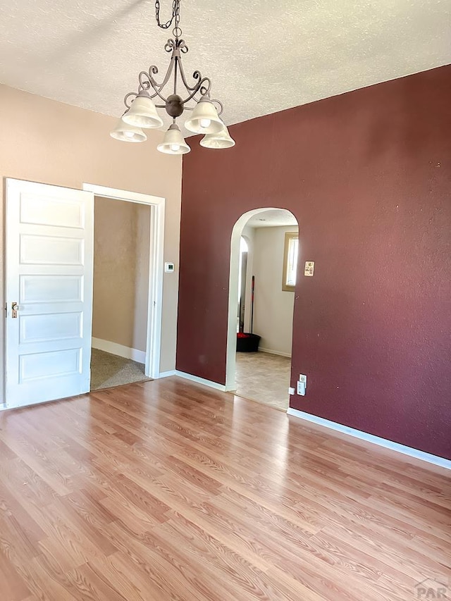 1202 Belleview Ave, La Junta, CO 81050 - empty room with a chandelier, arched walkways, light wood-type flooring, and a textured ceiling