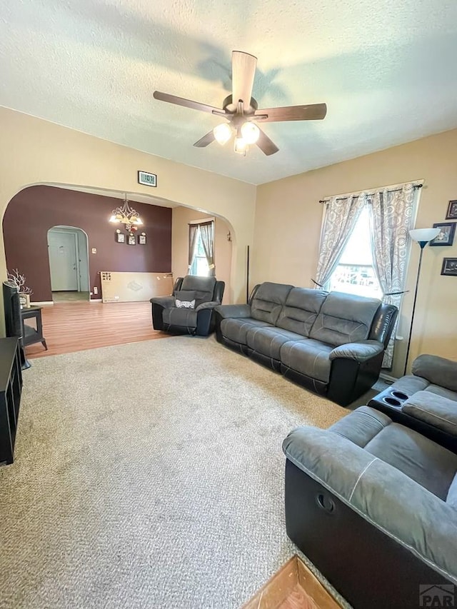 living area featuring arched walkways, a healthy amount of sunlight, a textured ceiling, and ceiling fan with notable chandelier