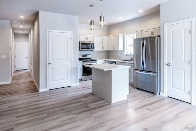 kitchen with a center island, stainless steel appliances, light countertops, hanging light fixtures, and a sink