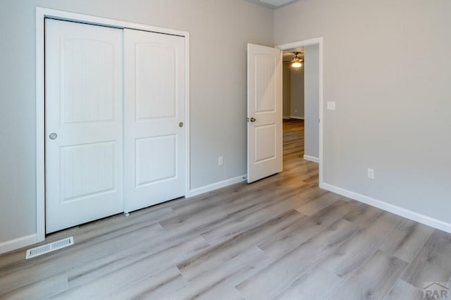 unfurnished bedroom featuring light wood-type flooring, baseboards, visible vents, and a closet