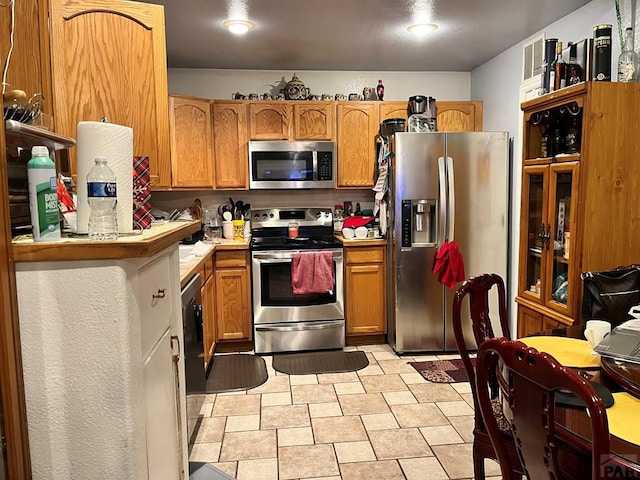 kitchen featuring stainless steel appliances, brown cabinetry, and light countertops