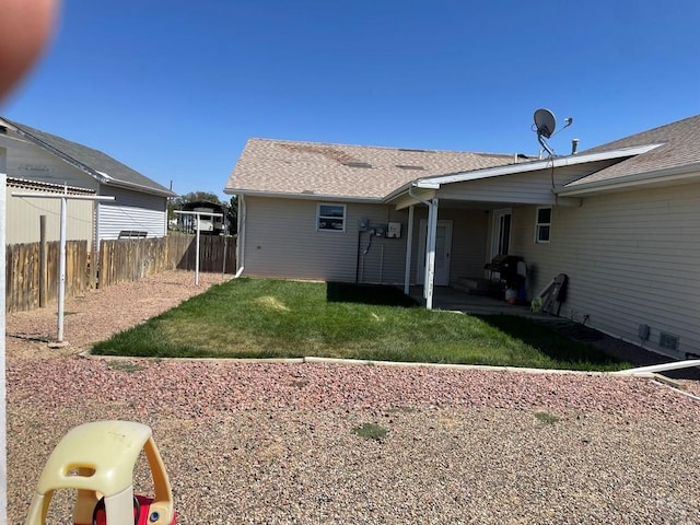 back of house featuring a shingled roof, a lawn, and fence