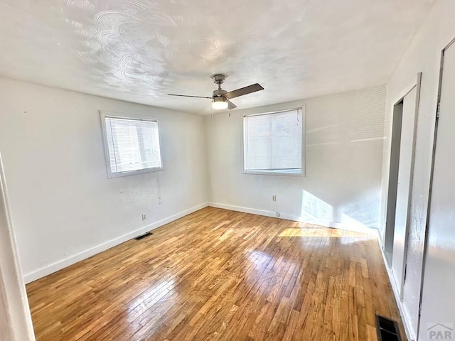 unfurnished bedroom with a ceiling fan, wood-type flooring, visible vents, and baseboards