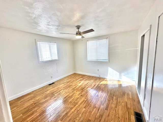 unfurnished bedroom featuring a ceiling fan, baseboards, visible vents, and hardwood / wood-style floors