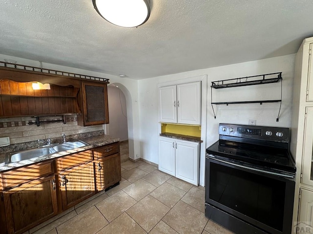 kitchen featuring arched walkways, a sink, black electric range, open shelves, and dark countertops