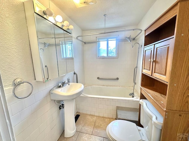 bathroom with toilet, tiled shower / bath combo, tile patterned flooring, a textured ceiling, and tile walls