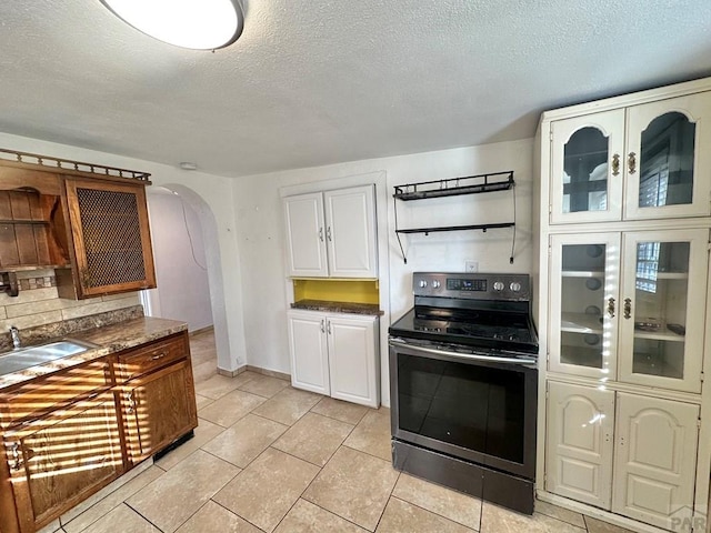 kitchen with arched walkways, a textured ceiling, range with electric stovetop, a sink, and white cabinets