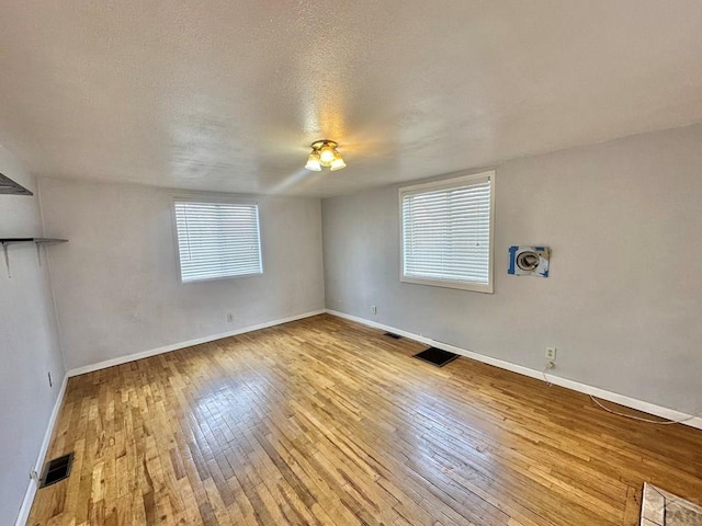 empty room with visible vents, plenty of natural light, baseboards, and hardwood / wood-style flooring