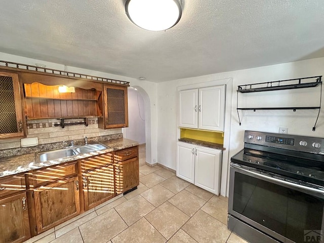 kitchen featuring arched walkways, a sink, stainless steel electric range oven, open shelves, and tasteful backsplash