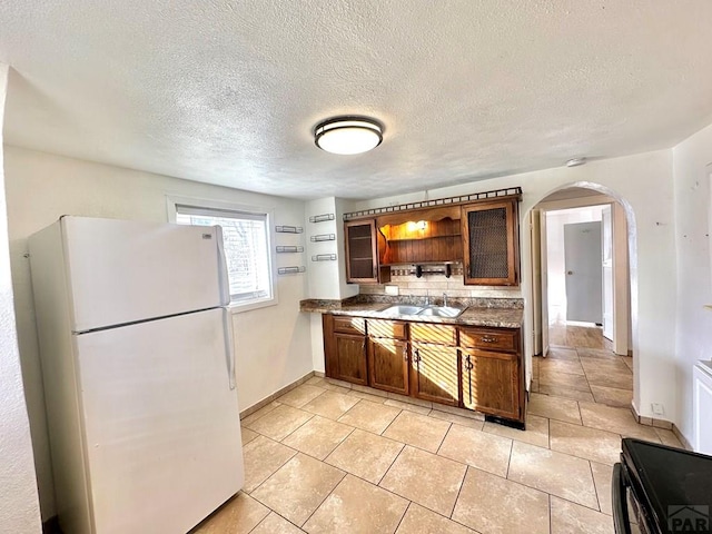 kitchen featuring arched walkways, dark countertops, freestanding refrigerator, open shelves, and a sink