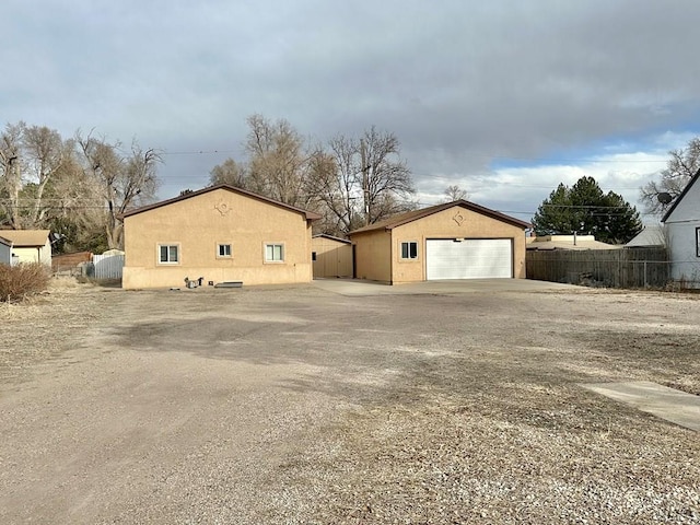 view of side of property with a detached garage, fence, an outdoor structure, and stucco siding