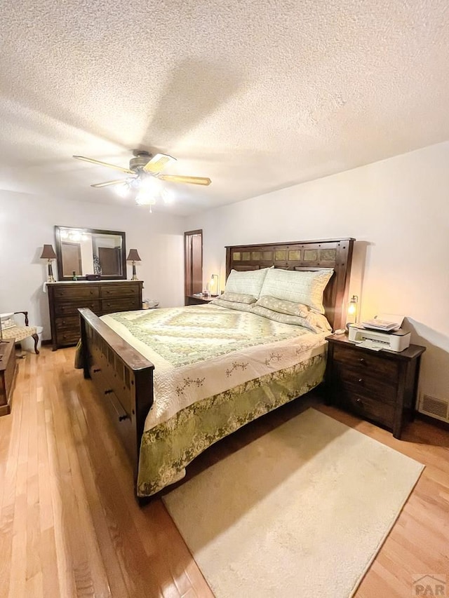 bedroom featuring light wood-type flooring, a textured ceiling, ceiling fan, and visible vents
