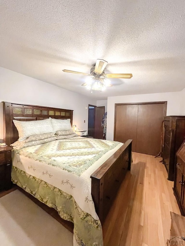bedroom with light wood-style flooring, a textured ceiling, a closet, and a ceiling fan