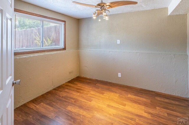 spare room featuring a ceiling fan, a textured wall, a textured ceiling, and wood finished floors