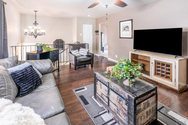 living room featuring dark wood-style floors, baseboards, and ceiling fan with notable chandelier