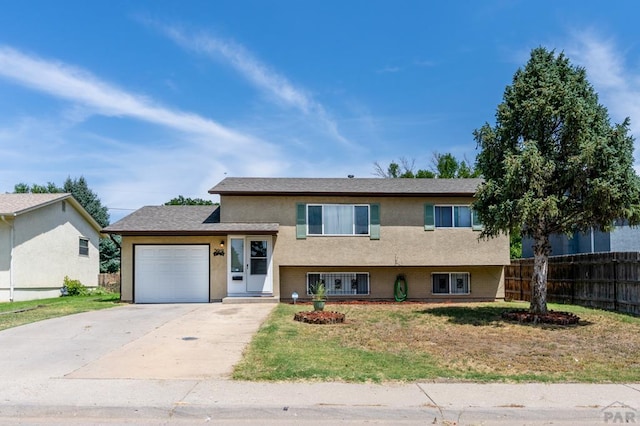 tri-level home with a garage, fence, driveway, and stucco siding