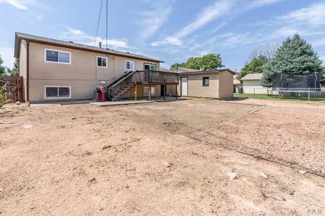 rear view of property featuring fence, stairs, a wooden deck, stucco siding, and a trampoline