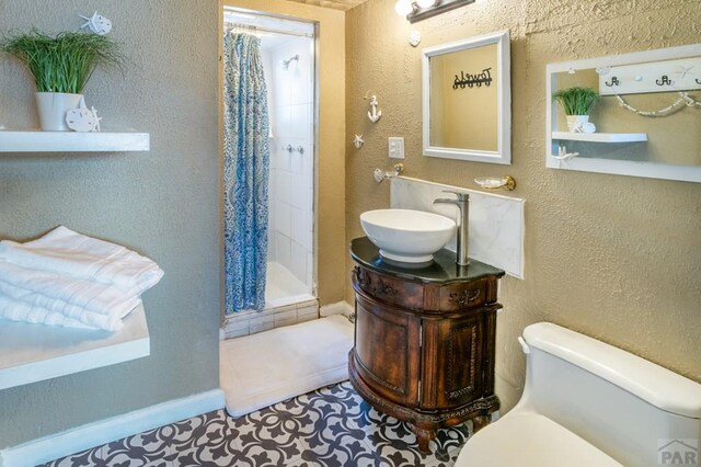 full bathroom featuring toilet, a stall shower, a textured wall, and vanity