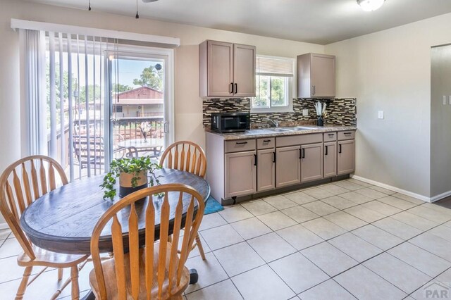 kitchen with light stone counters, backsplash, gray cabinetry, a sink, and baseboards