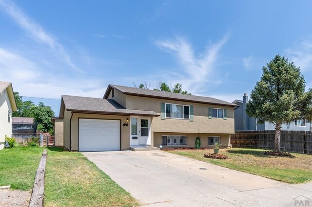 split level home featuring a garage, fence, concrete driveway, and stucco siding